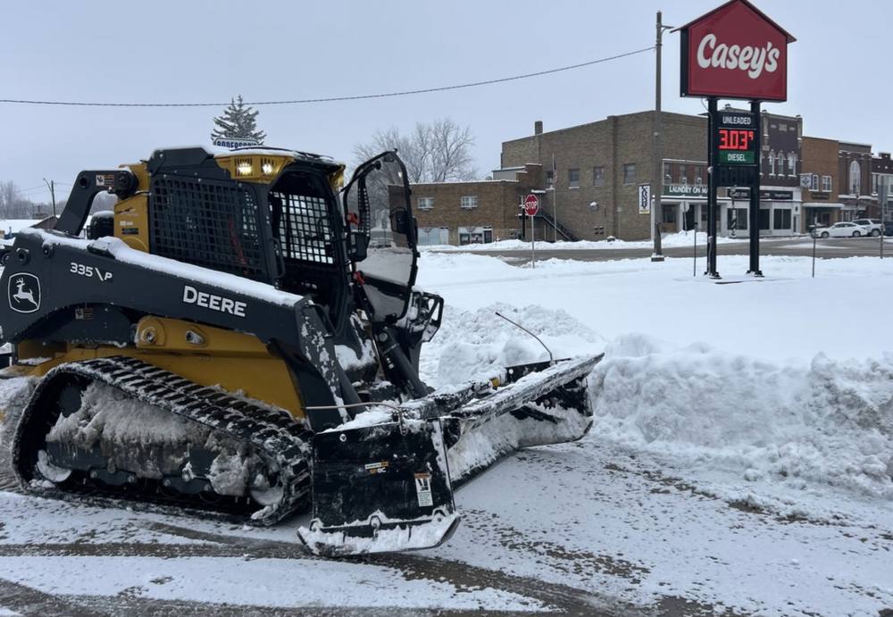 Skid steer with a plow blade clearing snow from a commercial lot